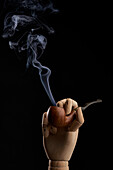 Traditional tobacco pipe with smoke in wooden hand on black background in studio