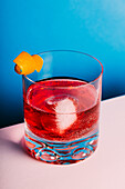 Glass of bitter alcoholic Negroni cocktail served with ice and orange peel on light surface