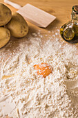 From above egg yolk placed on heap of wheat flour near potatoes and oil during gnocchi dough preparation on table in kitchen