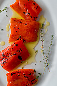 Draufsicht auf leckere gegrillte rote Paprikastücke mit frischen Thymianzweigen und Olivenöl auf Teller