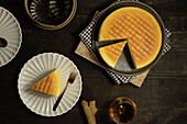 From above plates with tasty cotton cheesecake placed near glass of beverage on wooden table in dark room