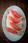 Hoher Winkel von Scheiben einer reifen süßen Wassermelone auf einem Keramikteller auf einem Holztisch vor dunklem Hintergrund