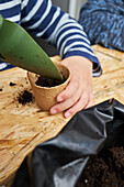 Crop anonymous kid with gardening shovel filling eco cup with earth at table