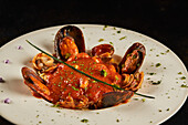 From above closeup seafood spaghetti with tomato sauce served on plate on black background in restaurant