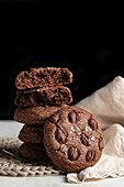 Ein Stapel Schokoladen-Roggenkekse auf einem Weidenteller neben einer Serviette auf weißem Hintergrund