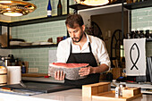 Focused male chef cutting raw fish at table in Asian restaurant and preparing sushi