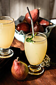 Glasses of delicious refreshing drinks with pear juice and fresh elderflower leaves on table