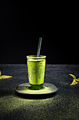 Healthy herbal green matcha tea served in glass cup with metal decoration on saucer sprinkled with powder on black table