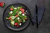 Dish with a summer salad of strawberries and cucumber on a dark table