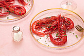 From above glass plate with tasty fried tiger shrimps placed near glass of wine on table pink background