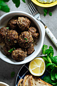 Top view of appetizing traditional homemade fried Greek meatballs served on gray background near plate with bread and lemon in kitchen