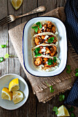 From above cauliflower snack tacos in bowl and lemon pieces in plate on wooden table