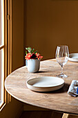 Servierter Tisch mit Keramiktellern mit Besteck auf Serviette neben Weingläsern und Blumen mit Früchten