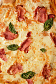Nahaufnahme einer leckeren hausgemachten Pizza mit Basilikum und Schinken, die auf einem Tisch serviert wird