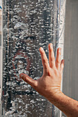 Crop anonymous person with hand placed on glass transparent surface with baubles in water