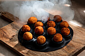 High angle of tasty roasted cheese balls in baking dish on wooden cutting board in kitchen in ice steam