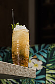 Tiki cup with cold alcohol drink with straw served with ice and decorated with fresh herb placed on blurred background