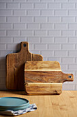 Wooden chopping boards placed near wall on table with bowl in light kitchen