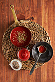Draufsicht auf Pfanne und Behälter mit köstlicher hausgemachter Tomatensauce mit Oregano bestreut auf gewebter Matte auf Holztisch in Küche