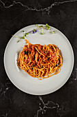Top view of yummy spaghetti alla puttanesca dish with tomato sauce and seafood garnished with garlic and chili pepper and served on plate in Italian restaurant