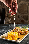 Unbekannter Koch streut Krümel auf Reis neben Ossobuco-Kalbfleisch, das auf einem Teller mit Blumen in einem Restaurant serviert wird