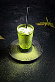 High angle of glass with cold green matcha latte with milk served with straw on saucer on black table