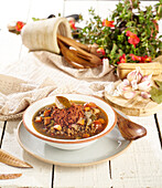 High angle of white bowl and plate with delicious lentil soup with vegetables placed on wooden surface near tableware