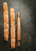 Top view composition with two artisan bread loaves placed near wooden rolling pin on black background
