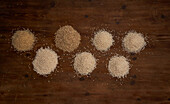 Top view of arranged small heaps of organic grains on wooden table near sickle and bunch of wheat