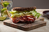 High angle of appetizing sandwich with fresh crusty bread above lettuce leaves and bacon on wooden board