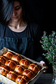 Female baker holding puff freshly baked hot cross buns on baking tray