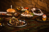 Appetitliche vegetarische Gerichte mit sautierten Pilzen und Gemüse neben Burger und Eis mit French Toast auf Holztisch