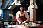 Young serious chef man in cooking apron serving meal in dishes on restaurant kitchen