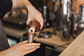 High angle of crop anonymous male barista in apron filling stainless jigger with sweet syrup while preparing beverage at counter in coffee house