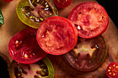 High angle of sliced tomato with salt placed on wooden chopping board among ripe red tomatoes with water drops