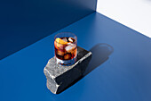 von oben Glas alkoholischer Cocktail mit rotem Wermut, serviert mit Orangenscheiben auf Stein in hellem Studio mit blauer und weißer Wand