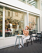 French female in beret sitting at table in cafe with aromatic glass of coffee and freshly baked croissant