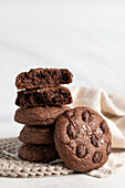 Pile of chocolate rye cookies placed on wicker plate near napkin on white background