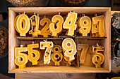 Draufsicht auf verschiedene bunte Kerzen in Form von Zahlen in einer Holzkiste auf einem Ladenregal