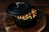 Hoher Blickwinkel auf einen Haufen Getreidekörner in einem schwarzen Topf mit Deckel, der auf einem Holztisch in der Küche steht