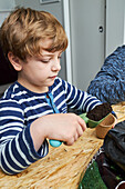 Kid with gardening shovel filling eco cup with earth at table