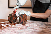 Soft focus of anonymous man using silicone spatula to remove excess chocolate from roller while preparing dessert during work in confectionery