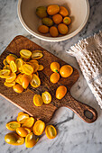 Top view pile of fresh orange cut kumquats on wooden chopping board placed on marble table with towel in kitchen
