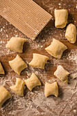 Top view of pieces of soft raw dough placed on wooden table covered with flour near ribber board during gnocchi preparation in the kitchen