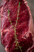 Overhead view of uncooked meat piece with thyme leaves against baking paper