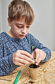 Child planting green seedling in cardboard cup with earth at table in house in daytime