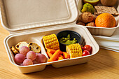 From above of lunch boxes with healthy food including crackers carrot sticks grapes cherry tomatoes with kiwi broccoli walnut and tangerine on yellow background