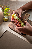From above of crop anonymous client of restaurant eating tasty sandwich made with bacon toasts and lettuce leaves with water with lime