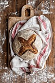 Top view of messy wooden rustic table in wheat flour and board with freshly baked sourdough bread loaf