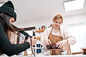 Crop anonymous photographer with photo camera against blogger with muffins in baking cups at home